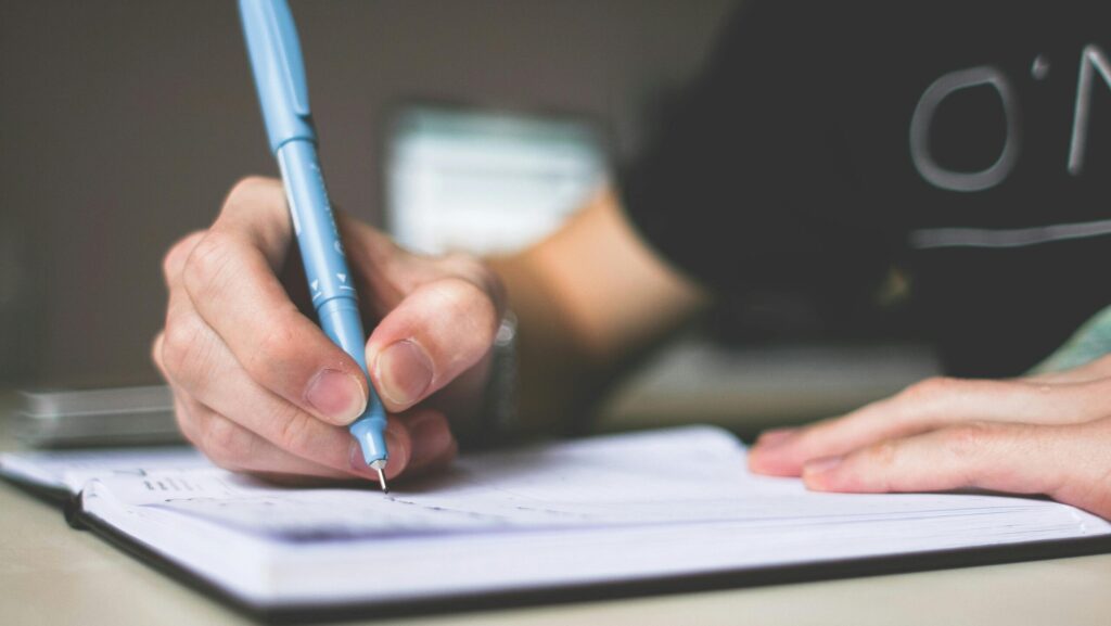 Close-up of hand writing in notebook using a blue pen, focus on creativity.